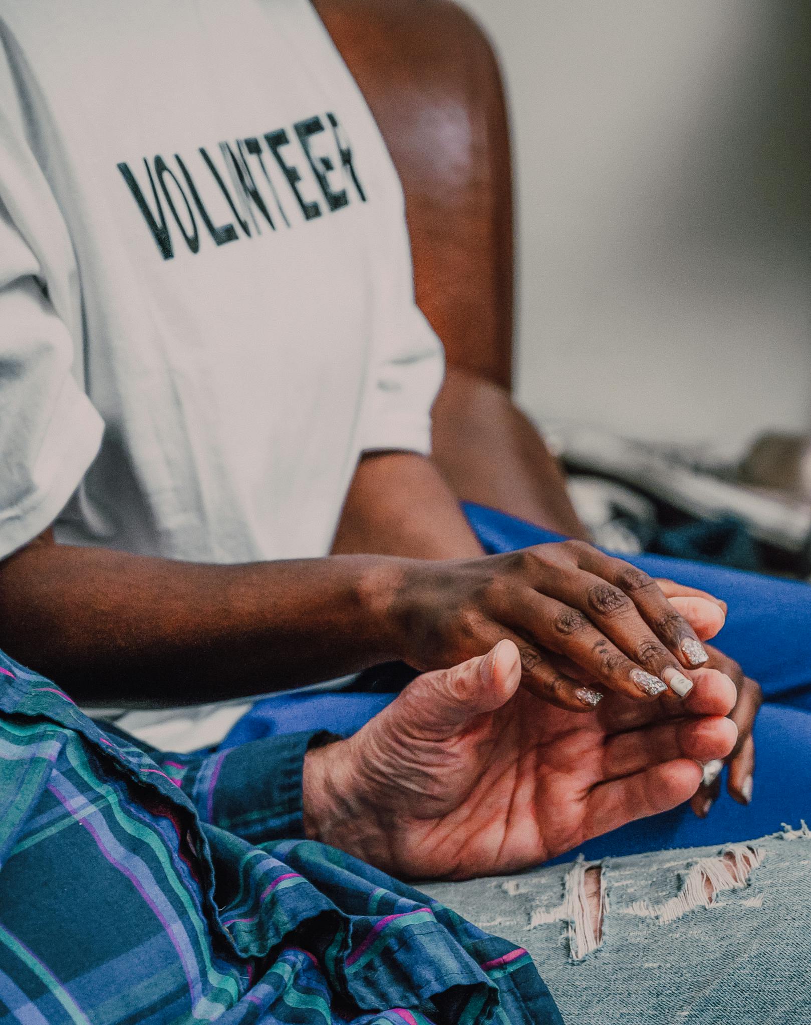 A volunteer offering comfort by holding hands with an elderly person, showcasing compassion.