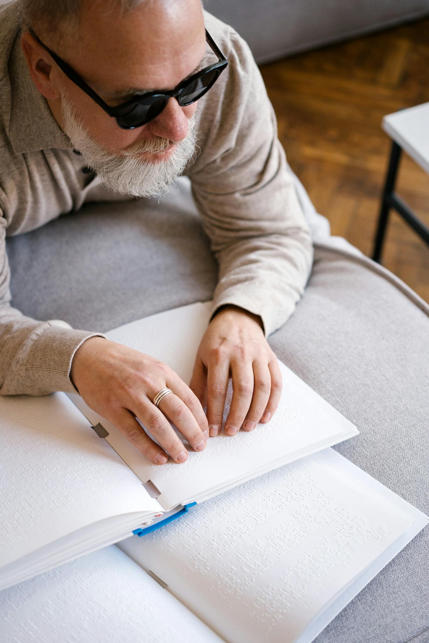 Man wearing sunglasses reading a Braille book, representing disability support and education.